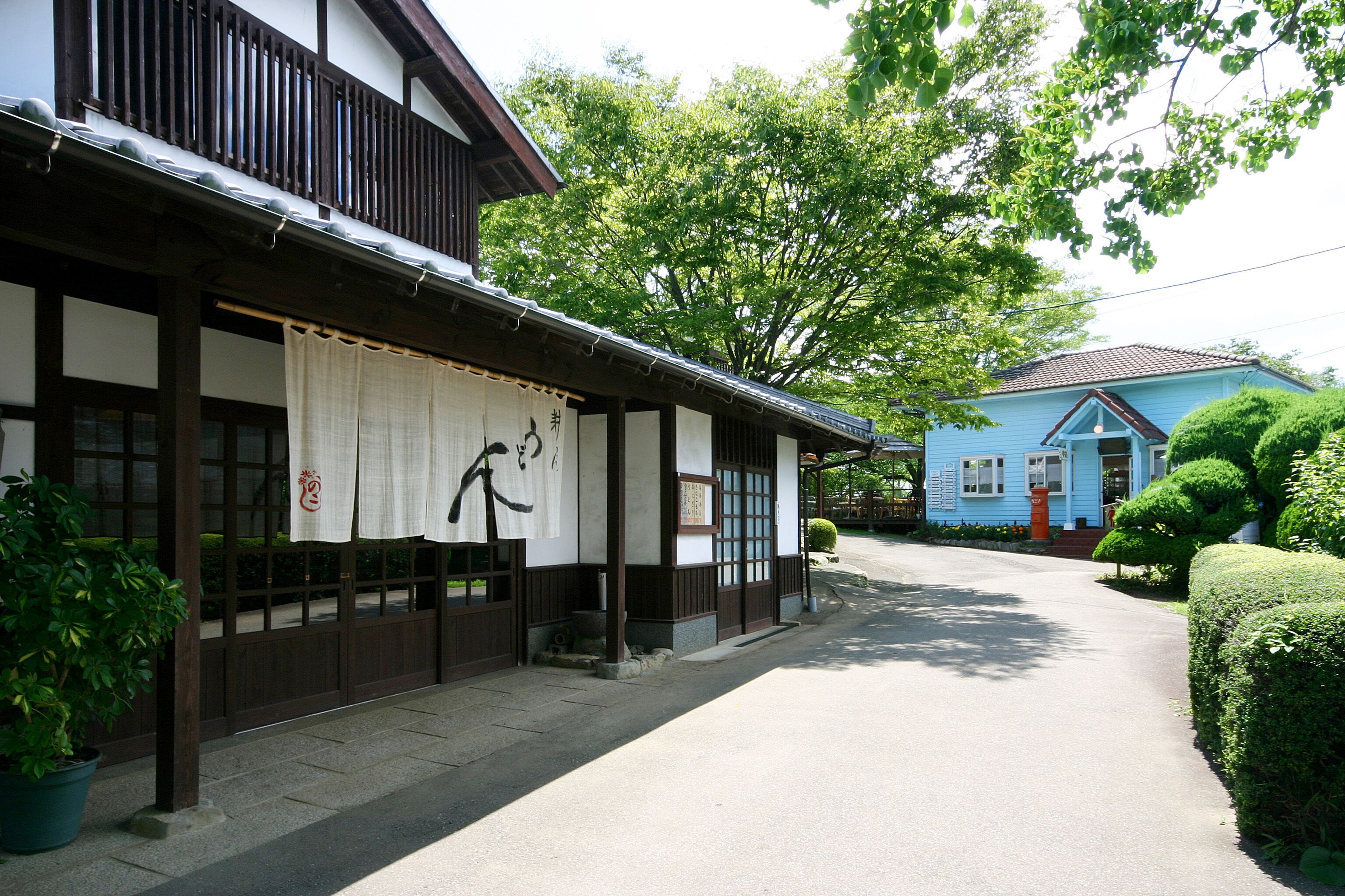 Un edificio japonés tradicional con fachada de madera y una casa azul al fondo.