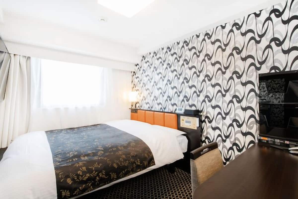 Une chambre d’hôtel avec un lit, un bureau, une télévision et un mur décoré d’un motif.