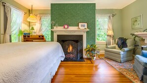 A bedroom with a fireplace, a bed, a chair, and a table with a lamp. - Howarth House B&B (Fitchburg)