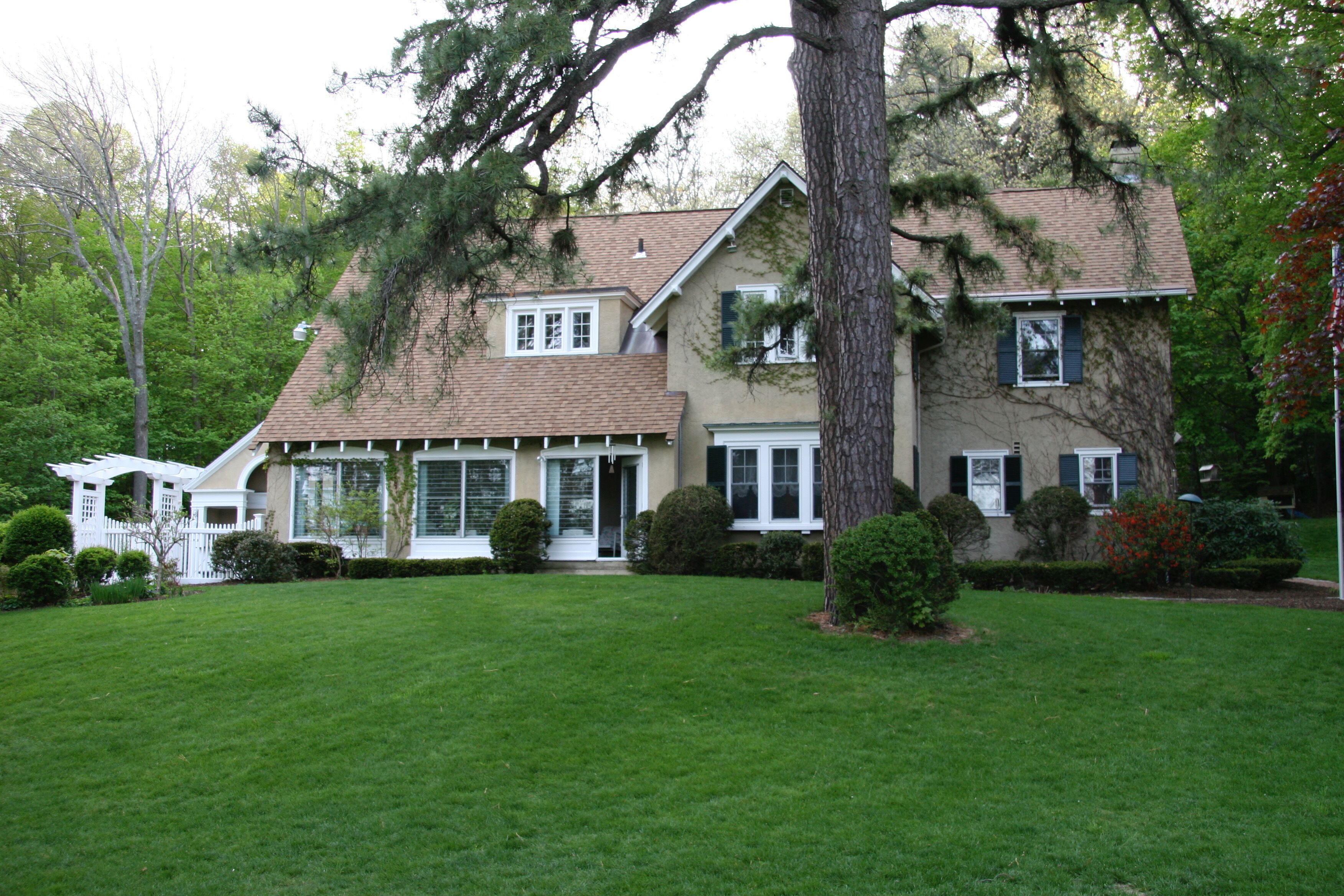 Une maison à deux étages avec une pelouse bien entretenue, un porche abrité et un grand arbre à l’avant.