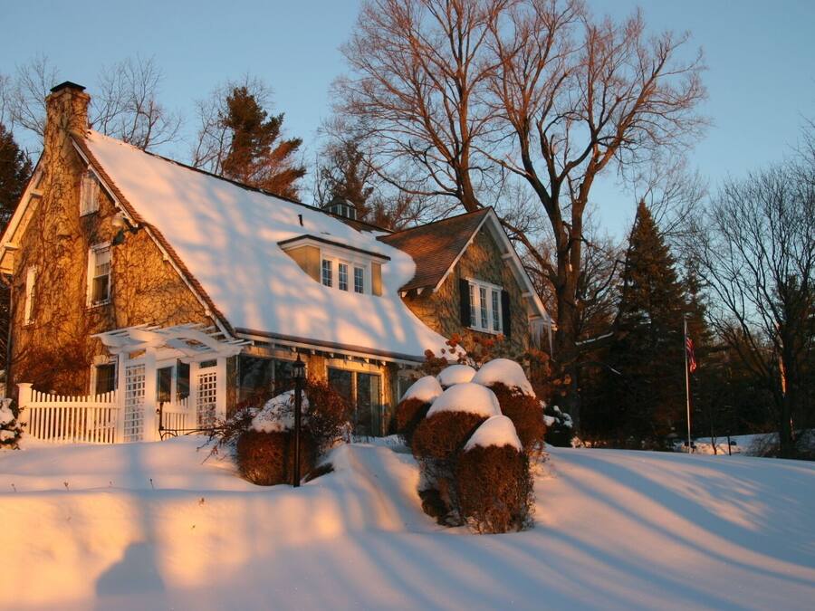 A stone house with a snow-covered roof and a white picket fence.