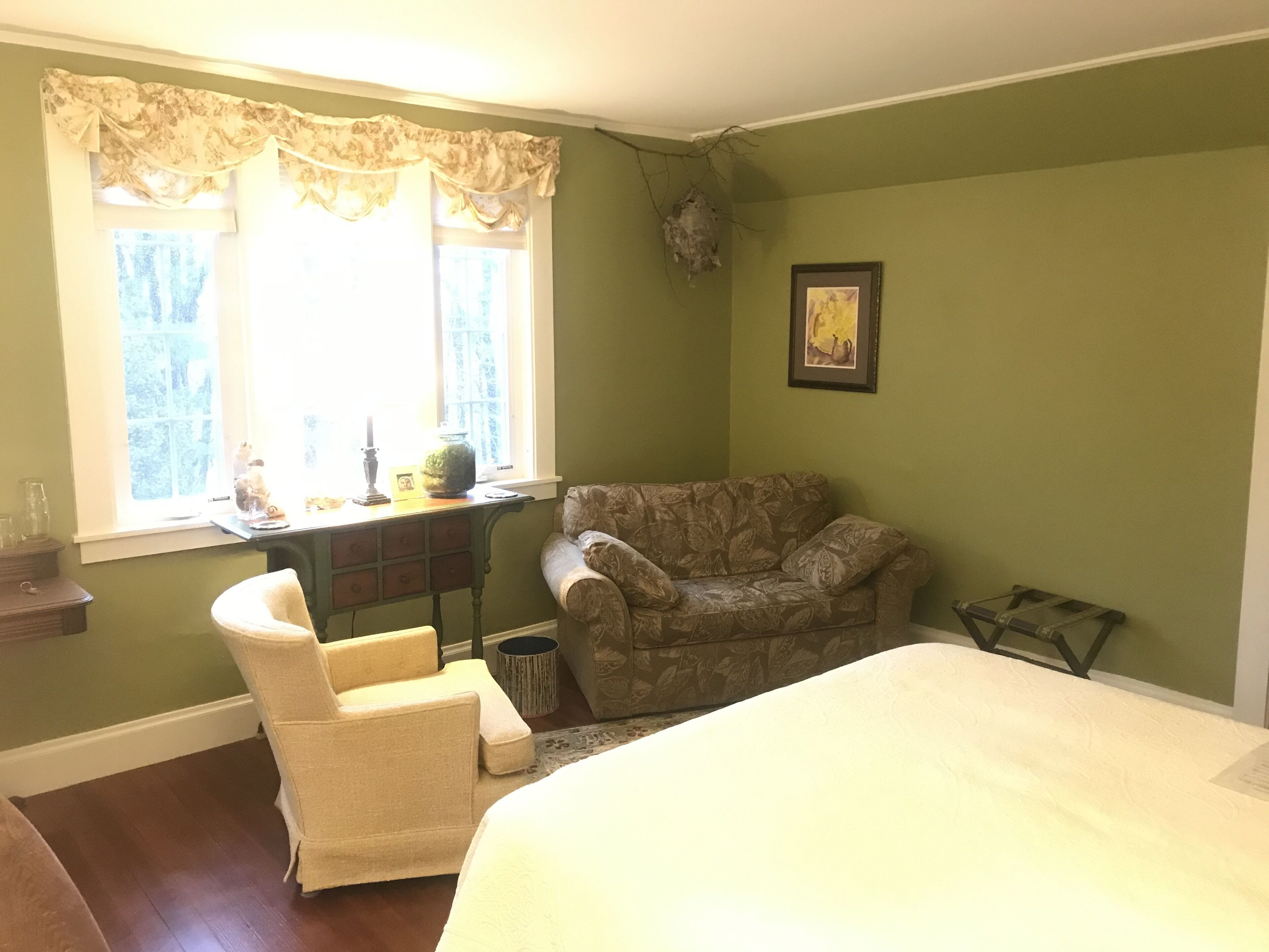 A bedroom with a bed, a chair, a desk, and a window with curtains.