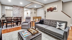 A spacious living room with a gray sofa, a coffee table, and a dining area with a wooden table and chairs.