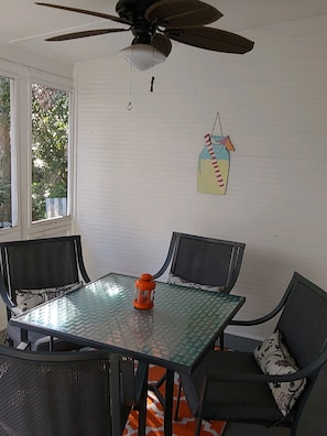 Et spiseområde med et bord og fire stole, en loftventilator og et vindue med udsigt til træer.