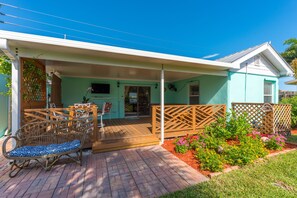 Relax on the covered patio with a wicker rocking chair and wooden table, surrounded by a beautiful garden.