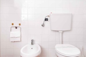 A bathroom with a toilet, bidet, and sink, featuring a towel rack with a folded towel.