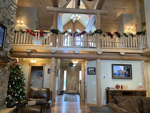 Cozy living area with leather sofa, smaller couch, and wooden table, surrounded by framed pictures and a Christmas tree.