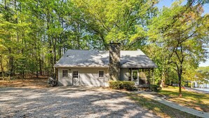 A house with a stone chimney, a front porch, and a gravel driveway surrounded by trees. - Private Dock & Beach! Lake Norman Cottage Hideaway (Mooresville)