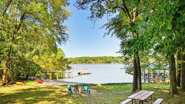 A lakeside picnic area with a wooden table and chairs, a canoe, and a dock extending into the water. - Private Dock & Beach! Lake Norman Cottage Hideaway (Mooresville)