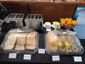 A breakfast buffet with labeled bread options, a fruit bowl, and a toaster. - The Bealey Hotel (Arthur's Pass)