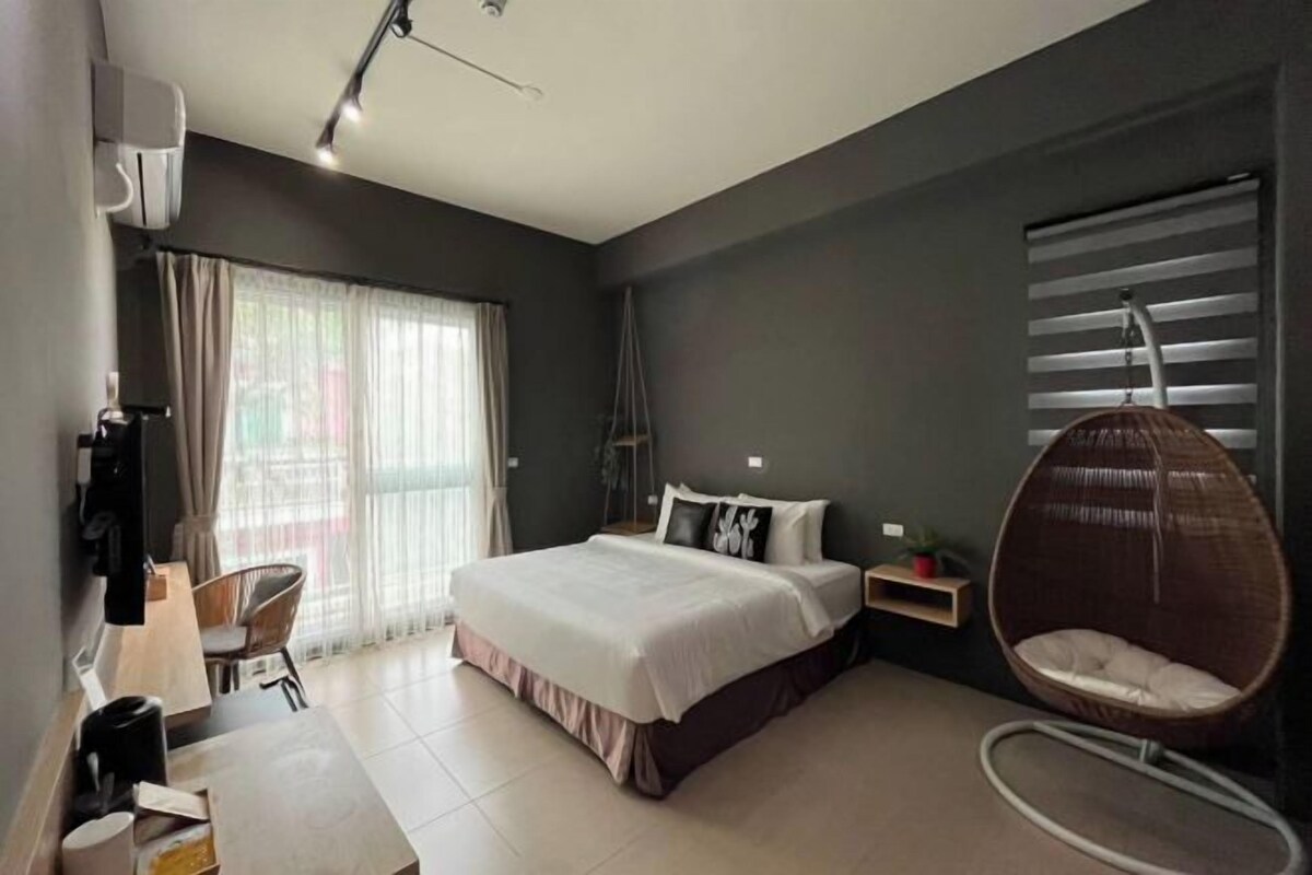 A modern bedroom with a large bed, a hanging chair, a desk with a chair, and a window with curtains.