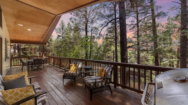 A wooden deck with outdoor furniture and a grill, overlooking a forested area. - Stunning Large Getaway with HOT TUB (Flagstaff)
