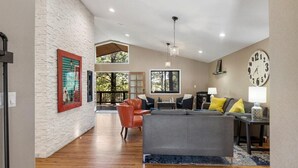 A spacious living area with a high ceiling, a large clock, and a view of the outdoors through large windows. - Stunning Large Getaway with HOT TUB (Flagstaff)