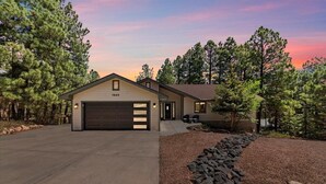 A single-story house with a garage, surrounded by pine trees, and a gravel driveway. - Stunning Large Getaway with HOT TUB (Flagstaff)