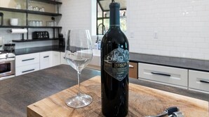 A bottle of wine and a glass on a wooden board in a modern kitchen with white cabinets and a brick backsplash. - Stunning Large Getaway with HOT TUB (Flagstaff)
