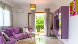 Ein modernes Wohnzimmer mit einem violetten Sofa, einem Fernseher und einem Balkon mit Vorhängen.