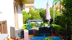 Eine Terrasse mit Gartenmöbeln, ein überdachter Bereich mit Pflanzen und eine Leiter.