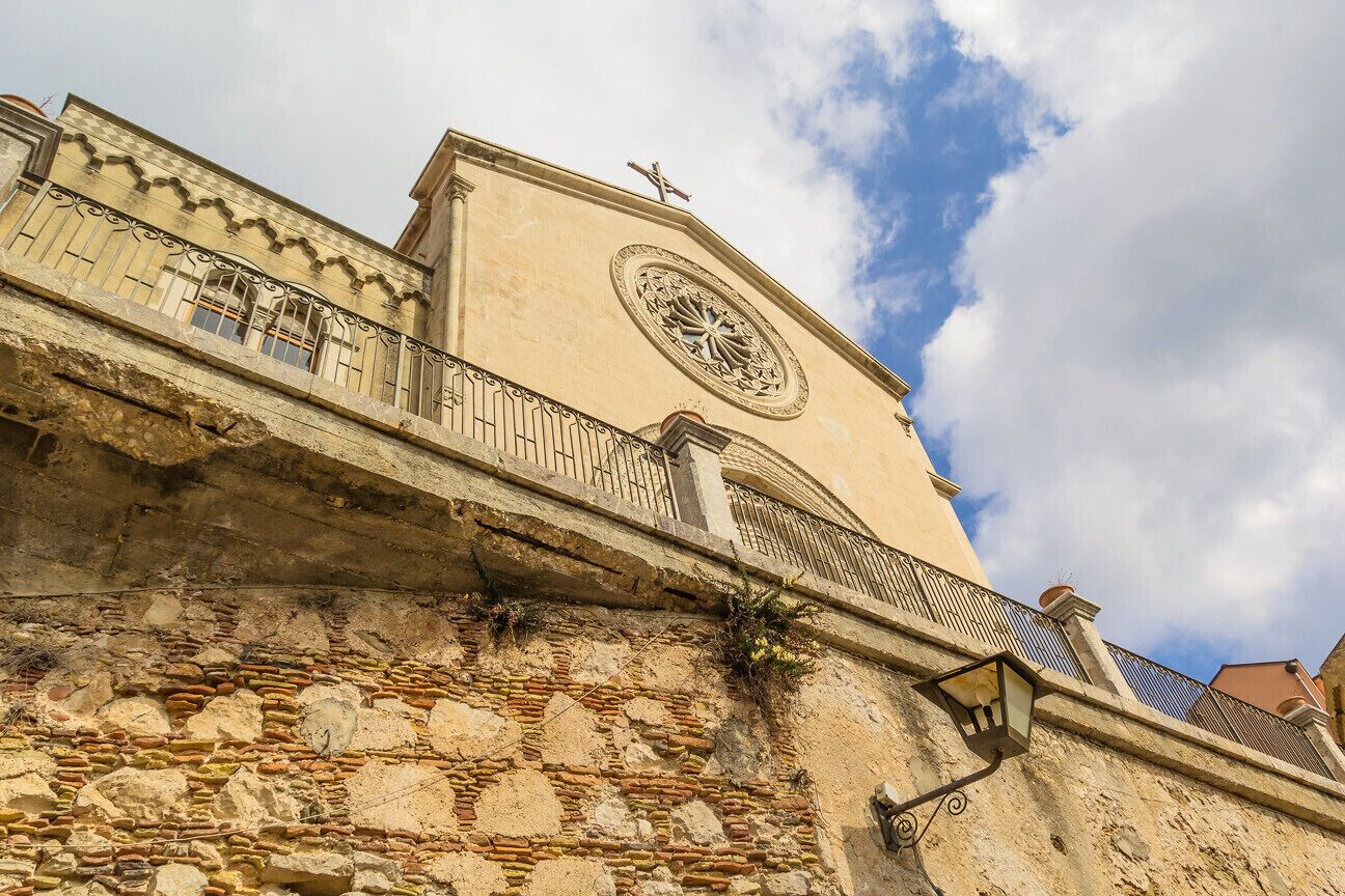Un edificio histórico con una torre de reloj, muros de piedra y un balcón con barandillas de hierro forjado.