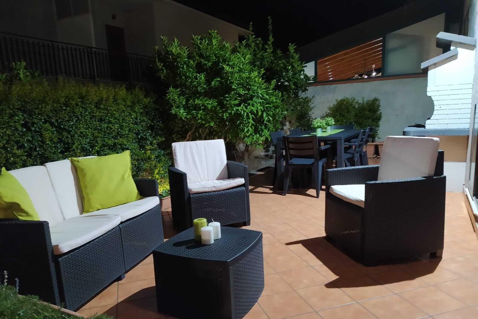 An outdoor patio area with wicker furniture, including a sofa and chairs, and a small table with candles.