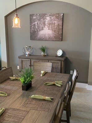 A dining area with a wooden table, chairs, a hanging light fixture, a wall-mounted clock, and a framed picture above the table. - 4 BED 3 BATH SUN KISSED LUXURY VILLA (Kissimmee)