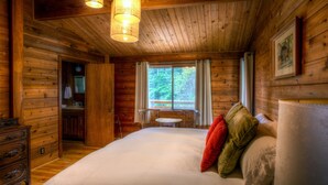 Un dormitorio de cabaña de madera con una cama grande, un aparador, una tocador y una ventana con vistas a árboles.
