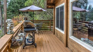 Una terraza de madera con una parrilla, asientos exteriores y sombrillas.