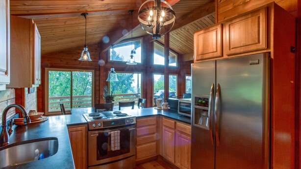 Una cocina moderna con armarios de madera, un refrigerador de acero inoxidable, un horno empotrado y un amplio ventanal con vista a una terraza.