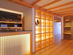 A reception area with a wooden reception desk, a wall with a geometric pattern, and a modern, open design with wooden beams and a slatted wall. - Hinasaku (Ito)