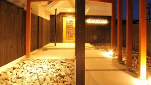 Eine Holzhütte mit einem Neonzeichen mit der Aufschrift „HINASAKU“ und einem Weg, der zu einer Tür führt.