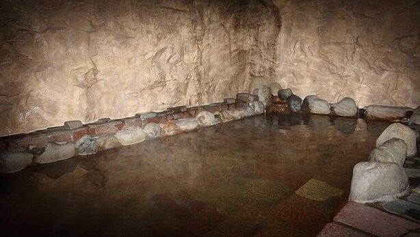 L’intérieur d’une grotte, avec une piscine bordée de pierres et un mur en briques.