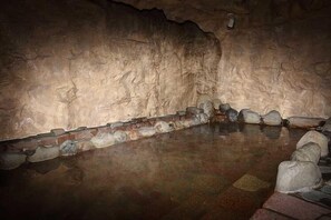 Interior de una cueva con una piscina revestida de piedra y una pared de ladrillo.