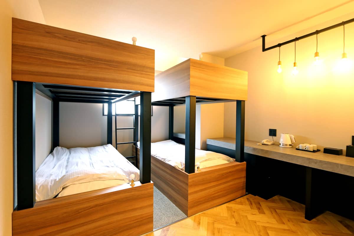 A modern hotel room with bunk beds, a wooden floor, a desk with a telephone and coffee maker, and a light fixture above.