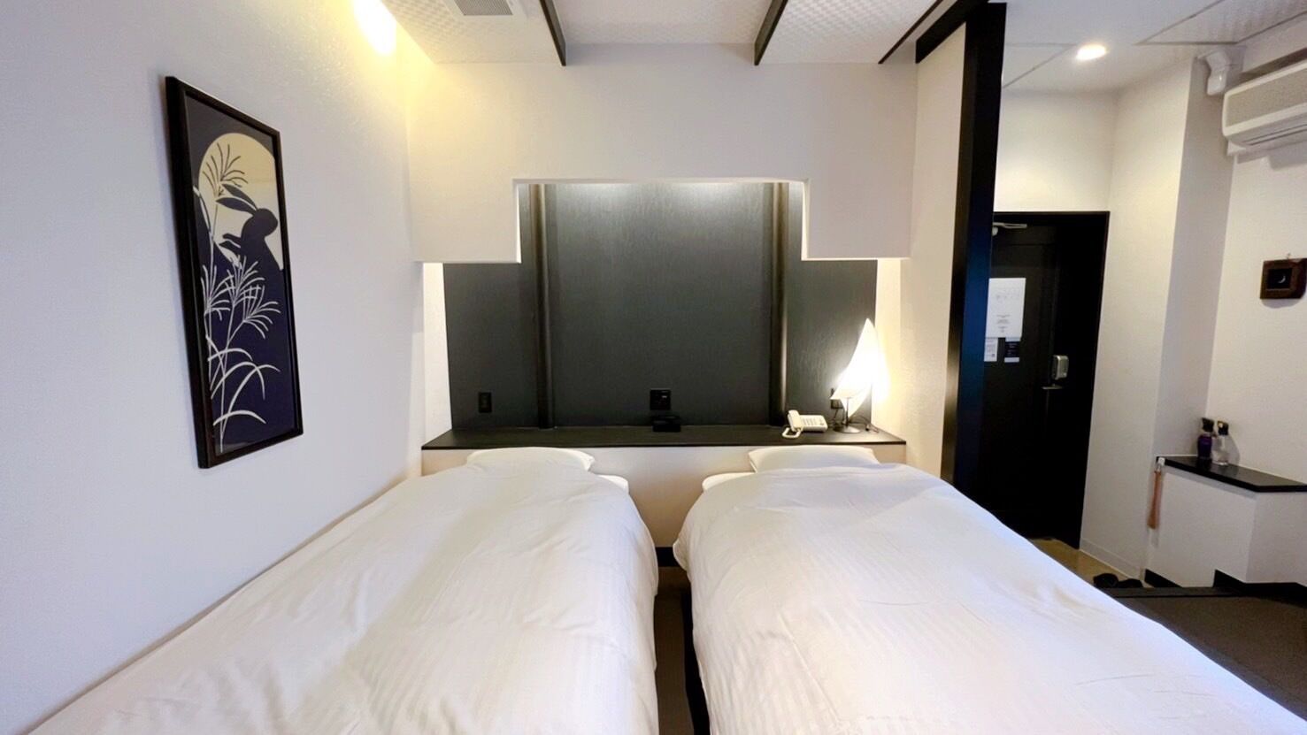 Camera d'albergo con due letti singoli, un grande specchio, un comodino con una lampada e un quadro appeso al muro.