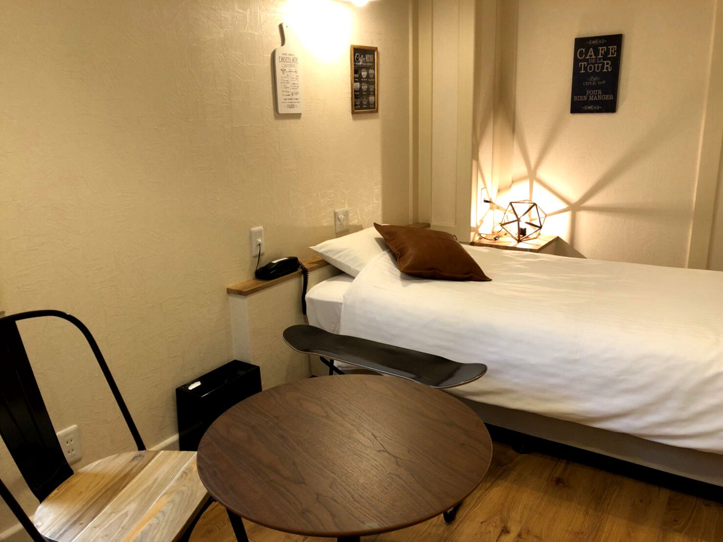A small, neatly arranged bedroom with a single bed, a bedside table, a chair, and a small round table.