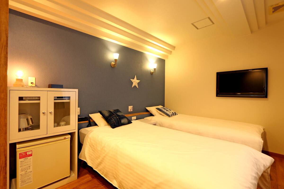 A hotel room with two beds, a minibar, a television, and wall-mounted lights.