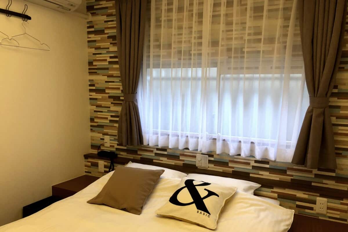 A hotel room with a bed, a window with sheer curtains, a wall-mounted coat rack, and a textured wall design.