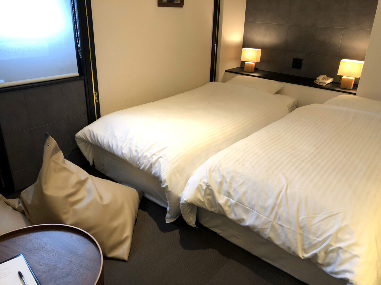 Et hotelværelse med to senge, et natbord med lampe, telefon og et lille bord med blyant.