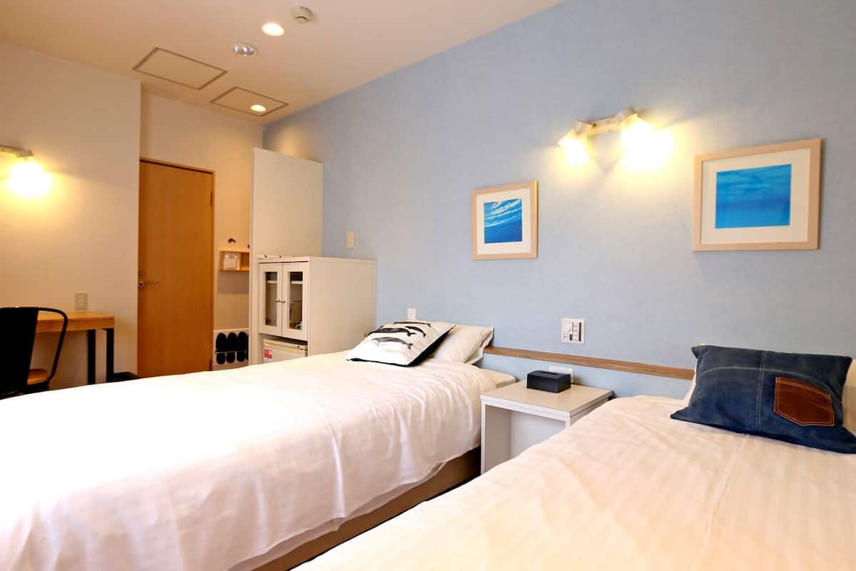 A hotel room with two beds, a desk, a chair, a wardrobe, and two framed pictures on the wall.