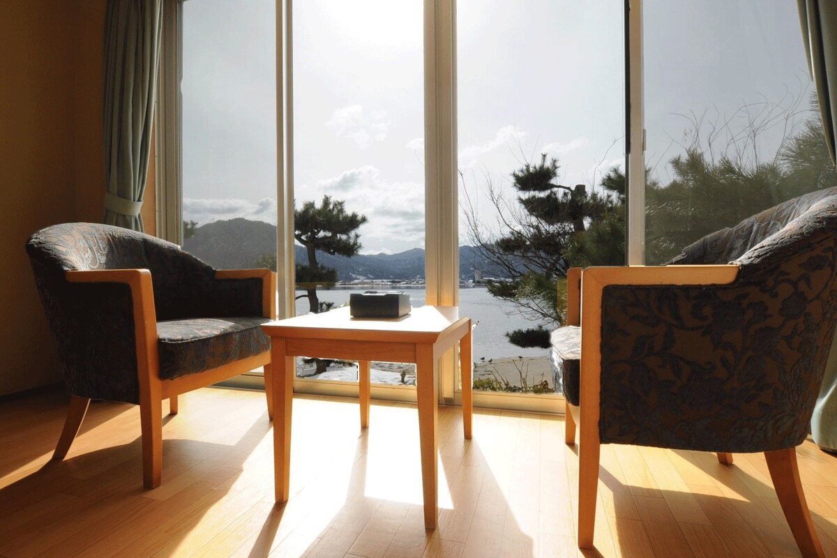 A room with two chairs, a small table, and a large window offering a view of mountains and trees.