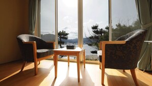 Una habitación con dos sillas, una mesa pequeña y un ventanal con vistas a montañas y árboles.