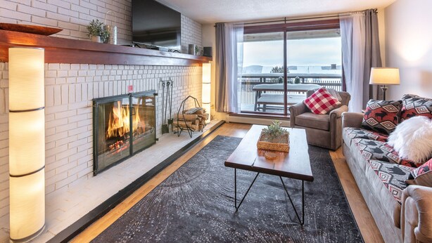 En stue med pejs, fjernsyn, sofa og udsigt til en balkon.