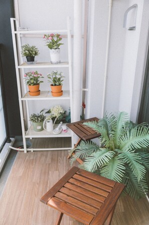 Un banco de madera, un estante blanco con plantas en macetas y una gran planta de helecho verde.