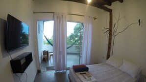 Un dormitorio con cama, televisor, ventana con cortinas y vistas al exterior.