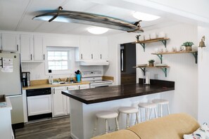 Una cocina con gabinetes blancos, encimera de madera e isla central con taburetes.