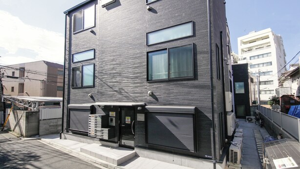 Een modern gebouw met twee verdiepingen, een plat dak, grote ramen en een zwart gevel.