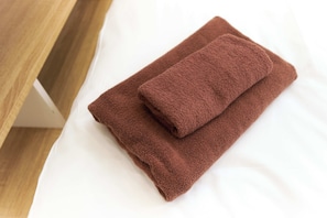 Een keurig opgevouwen bruine handdoek op een wit bed.