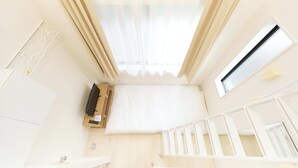 Een kamer met een dakraam, een klein raam, een wit wiegje en een houten kast.