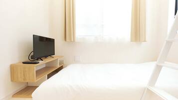 A room with a bed, a TV on a wooden shelf, and a window with curtains.