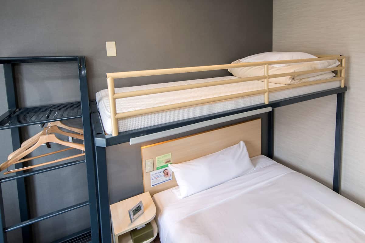 Ein Stockbett mit Holzbettrahmen, ein einzelnes Bett unten und ein Regal mit Kleiderhaken.