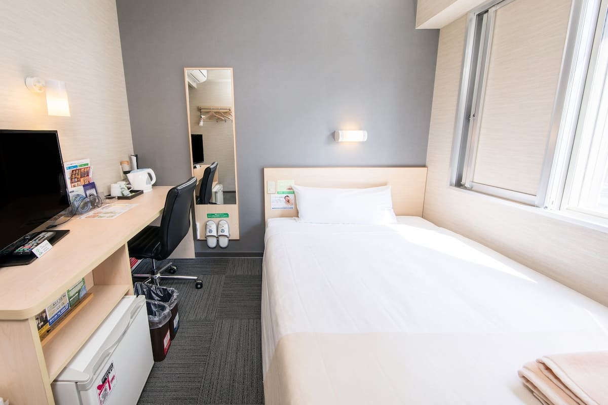 Ein Hotelzimmer mit Bett, Schreibtisch mit Computer, Stuhl, Spiegel und Fenster.